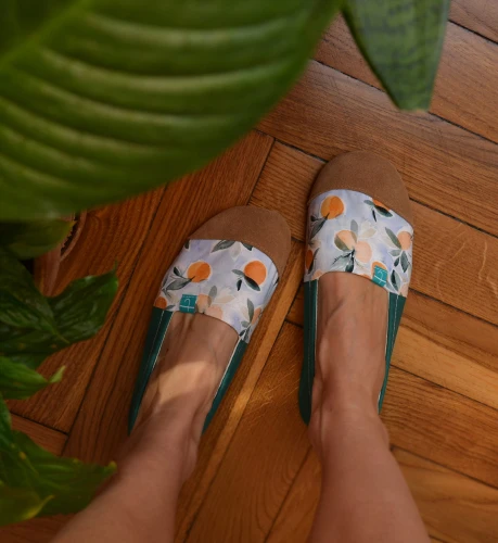 kobieta w kapciach damskich TITOT Watercolor Oranges siedzi na podłodze, ukazując jak kapcie dopasowują się do stopy