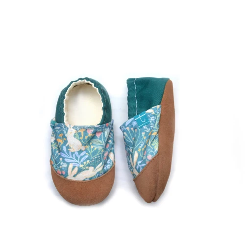 Zbliżenie na detal kapci dziecięcych Bunny, ukazujące uroczy wzór z zajączkami i delikatne przeszycia. Widoczna jest miękka, skórzana podeszwa barefoot oraz elastyczna gumka wokół kostki zapewniająca idealne dopasowanie.