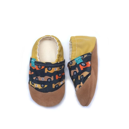 Dziecięcy bucik Titot w wzór Autka Wyścigowe, widoczna brązowa podeszwa ze skóry i musztardowo-żółta tkanina przy kostce.