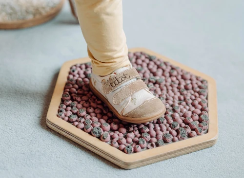 Stopa dziecka w trampku barefoot Titot Forrest Friends na desce z otoczakami