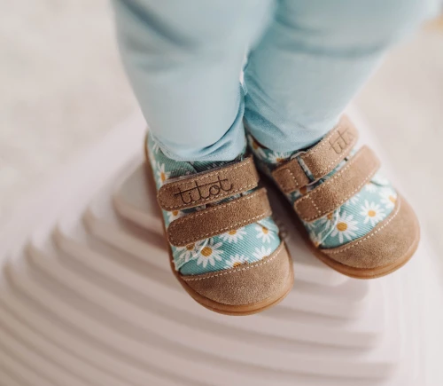 Zbliżenie na rzepy i skórzane noski niebieskich butów w stokrotki na stópkach dziecka.