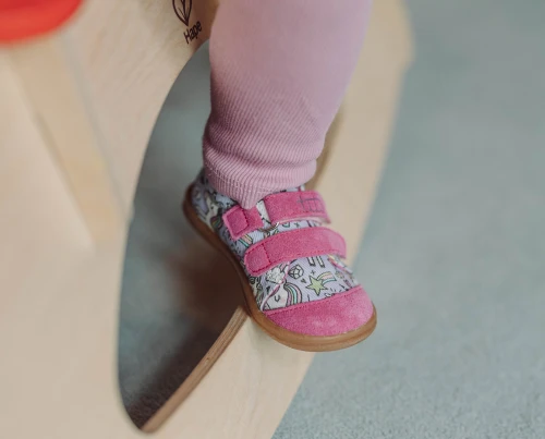 Dziecko siedzące na drewnianym koniku w trampkach Rainbow Unicorn i różowych legginsach.