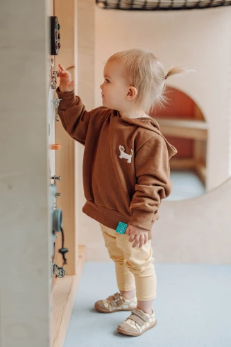 Dziecko w beżowych butach w stokrotki stoi przy siatce zabezpieczającej.