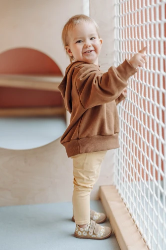 Uśmiechnięte dziecko w brązowej bluzie i beżowych trampkach w stokrotki.