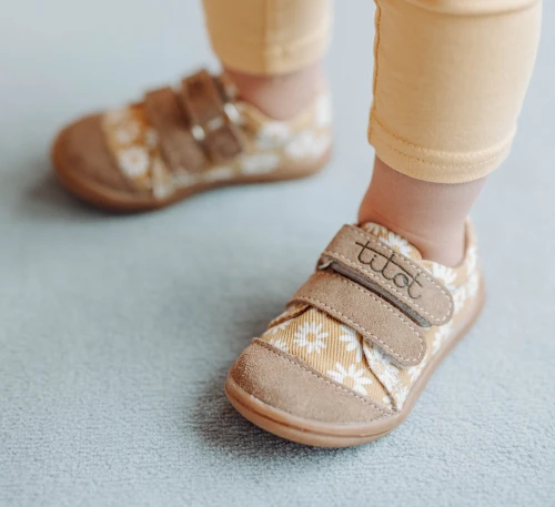 Beżowe trampki dziecięce Titot Beige Daisy w białe stokrotki na nogach dziecka.