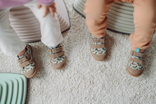 Zbliżenie na stopy dzieci w butach Hot Doggy odpoczywających na jasnym dywanie.