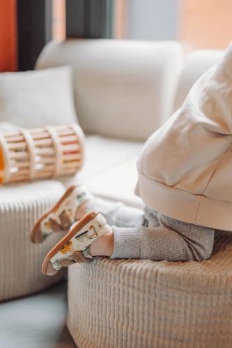 Stopy dziecka w butach City Builders podczas zabawy na pufie, widoczna kauczukowa podeszwa.