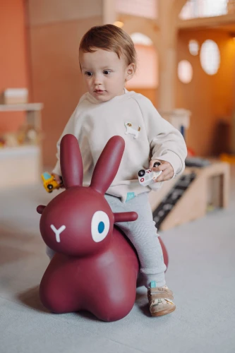 Dziecko na czerwonym skoczku w butach w koparki City Builders trzymające zabawkowe auto.