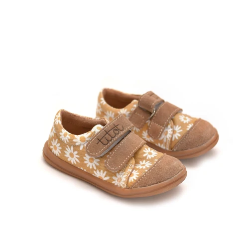Ustawione pod kątem stylowe buty dziecięce marki TITOT z motywem stokrotek na beżowym tle.